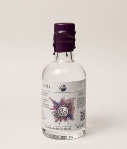 A 20cl gin bottle, with a dark purple wax style seal. The label is mostly white, with a picture of an armadillo in a burst of colour